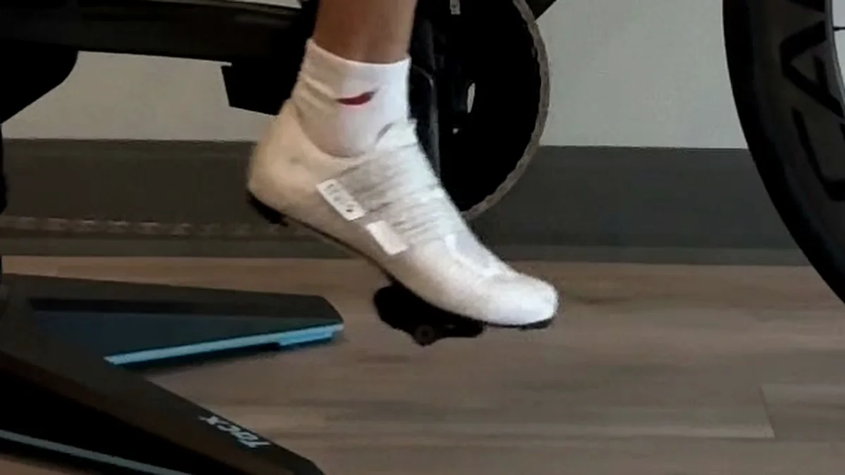 Close-up of a white cycling shoe clipped into the pedal at the bottom of the stroke