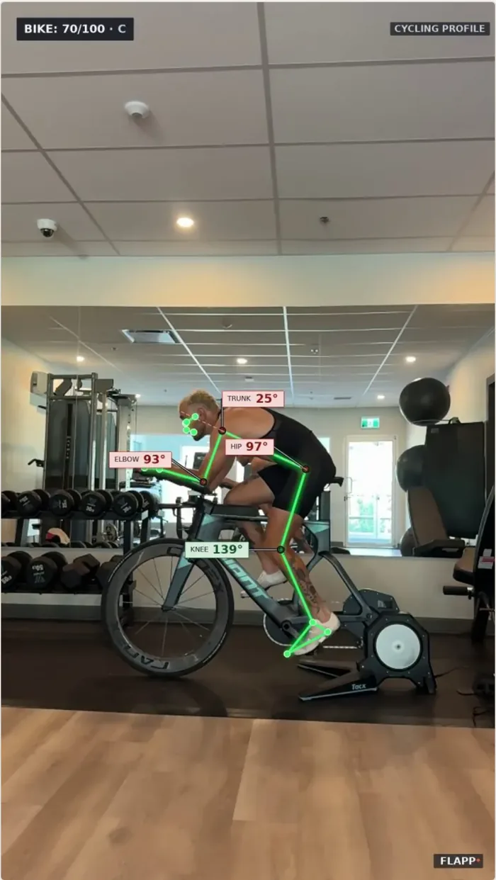 A road rider on an indoor trainer, filmed from the side, with the pose skeleton drawn on and the trunk, hip, elbow and knee angles labelled; the banner reads Bike 70 out of 100, C