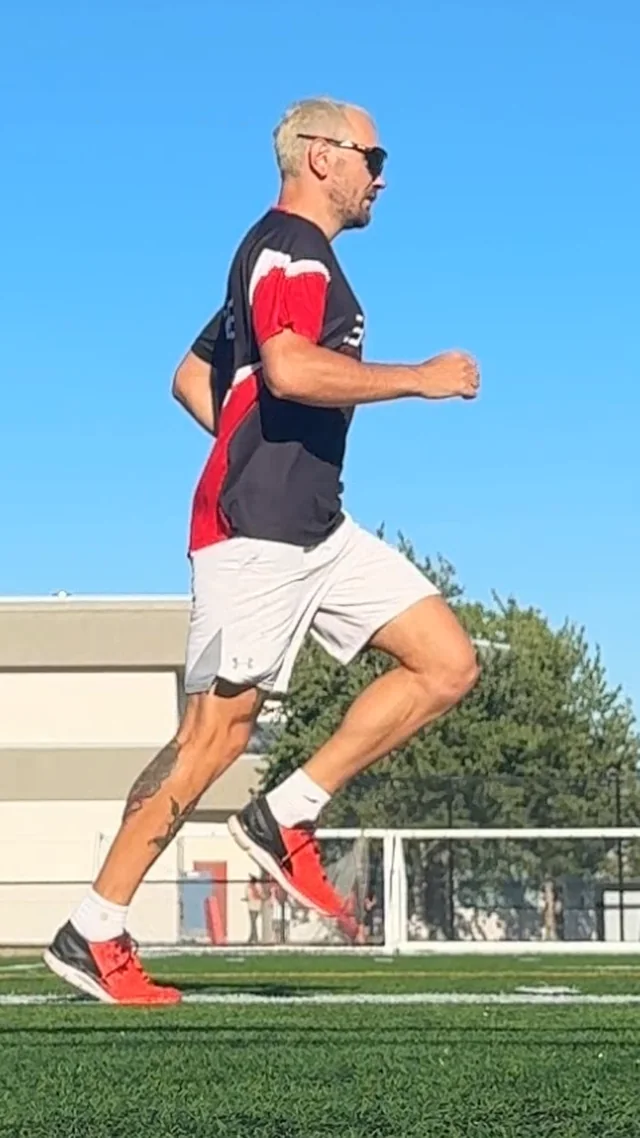 Side-view phone photo of a runner mid-stride on a sports field